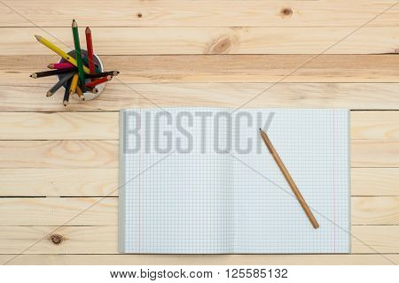 Open notebook with colored pencils on the wooden table.