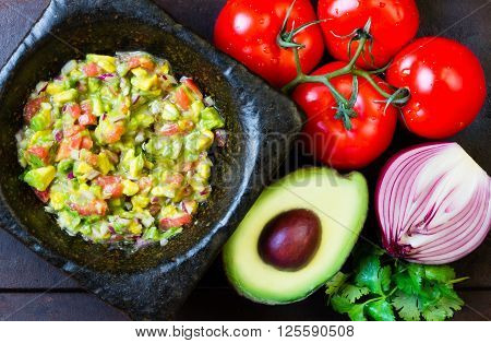 Guacamole - latin american mexican sauce in stone mortar and ingredients on dark background. Top view