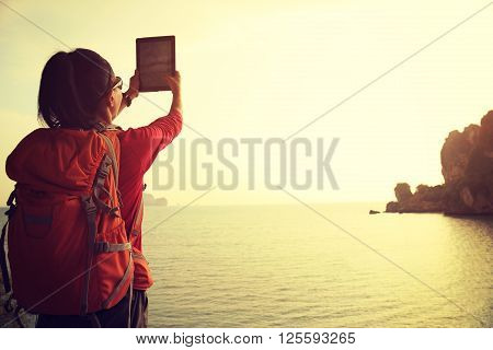 young woman hiker use digital tablet on sunset seaside