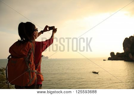 young woman hiker use smartphone taking photo on sunset seaside