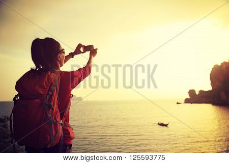 young woman hiker use smartphone taking photo on sunset seaside