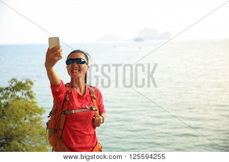 young woman hiker use smartphone taking photo on sunset seaside