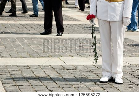 Lower body of officer in white uniform who holds carnation flowers on Victory Day celebration at the Museum of The History of Ukraine in World War II in Kyiv, Ukraine