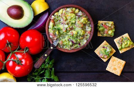Guacamole - latin american mexican sauce in stone mortar and ingredients on dark background. Top view