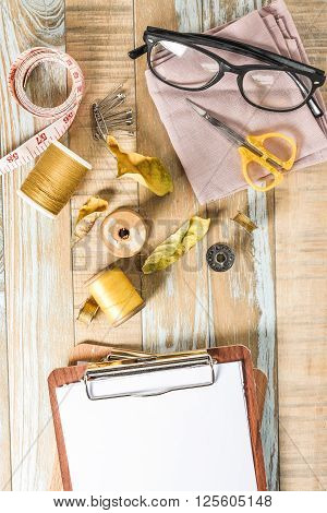 Blank clipboard and sewing kit on wooden textured background