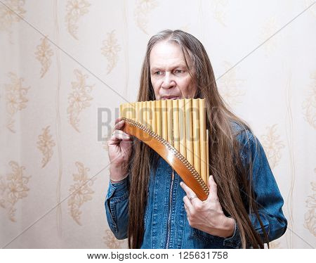 long-haired elderly man playing the pan flute closeup