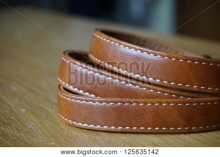 Brown leather band with white stitching on the wooden desk