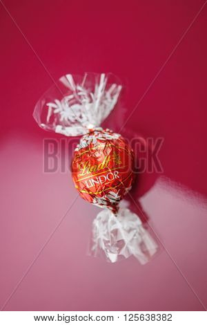 KILCHBERG SWITZERLAND - MARCH 20 2014: Lindt Lindor chocolate truffle on a red luxury silk background. Lindt is one one of the lastgest luxury chocolate and confectionery company worldwide with more than 30 factories worldwide