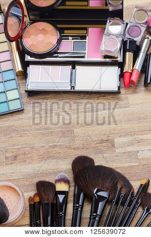 brushes, lipsticks, maskara, eye shadows and  powder on wood borders, top view with copy space