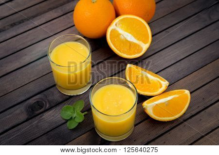 Freshly squeezed orange juice in glass, with fruits on wooden background