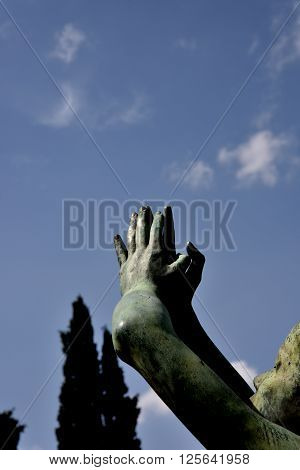 Hands of statue connected that pray upwards. Detail of face. On background blue sky