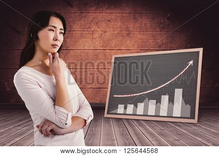 Thoughtful young woman with hand on chin against black board on wooden floor