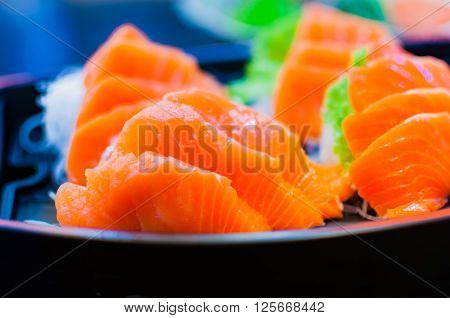 Selective focus of raw fresh sashimi serve in a boat bowl with green wasabi and sliced radish
