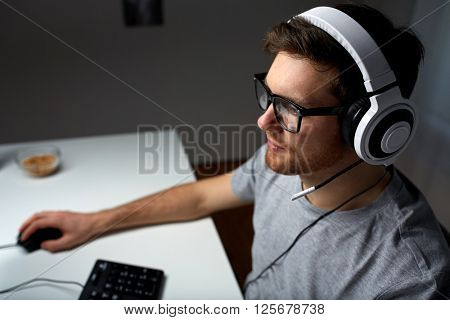 technology, gaming, entertainment, let's play and people concept - young man in headset and glasses with pc computer playing game at home and streaming playthrough or walkthrough video