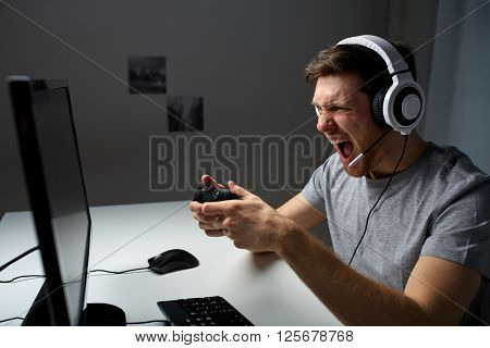 technology, gaming, entertainment, let's play and people concept - angry screaming young man in headset with controller gamepad playing computer game at home and streaming playthrough video