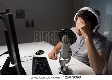 technology, gaming, entertainment, let's play and people concept - close up of sad young man in headset with pc computer playing game at home and streaming playthrough or walkthrough video