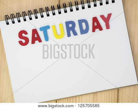Saturday word spell by wooden letters on blank notebook with wood background (Weekdays word series)
