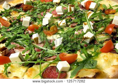 Appetizing pizza with ham, salami, arugula, cherry tomatoes, fetaksa, balsamic closeup