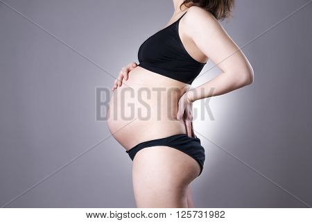 Caucasian pregnant woman in black lingerie with back pain on gray studio background. Pregnancy concept