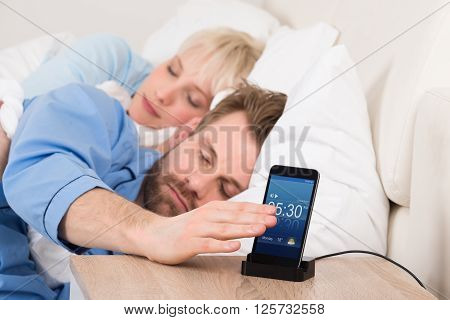 Man On Bed Snoozing Alarm Clock On Cell Phone Screen While Sleeping