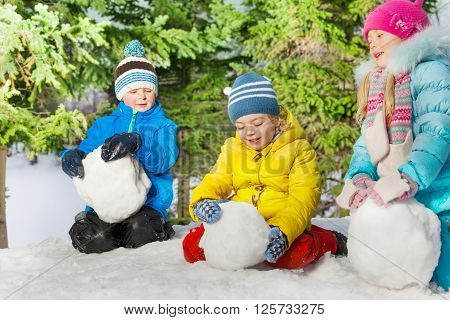 Group of kids roll snow ball in the forest at winter