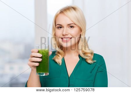 healthy eating, vegetarian food, diet, detox and people concept - smiling young woman drinking green vegetable juice or smoothie from glass at home