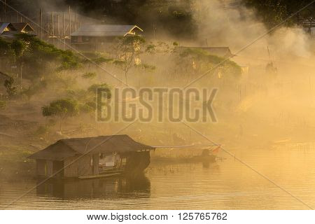 Misty tropical sunset on lake with boat and wooden home in Sangklaburi, Thailand