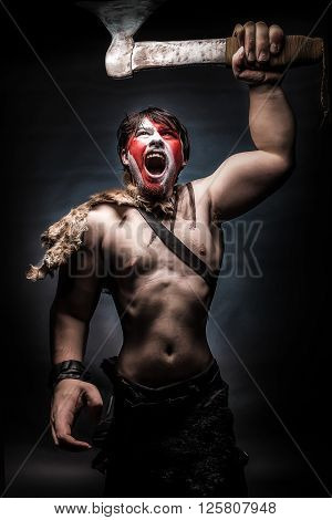 Painted image of man in war paint with an ax in his hand a warrior brandishing an ax furiously screaming barbarian of ancient times Viking and savage.