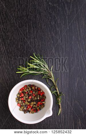 a mixture of peppers ( red black white ) in a white mortar with a sprig of rosemary