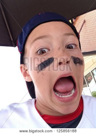 Cute baseball boy close up with backwards hat and mouth wide open.