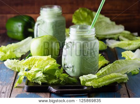 Two glasses of green smoothie and fresh green vegetables and fruits on wooden blue background