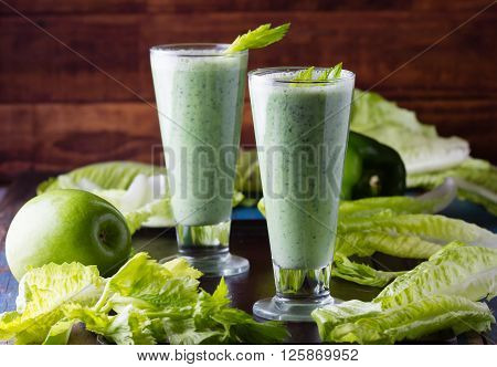 Two glasses of green smoothie and fresh green vegetables and fruits on black background