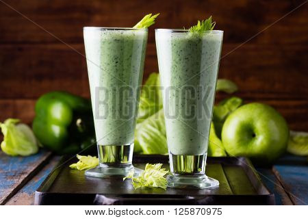 Two glasses of green smoothie and fresh green vegetables and fruits on wooden blue background