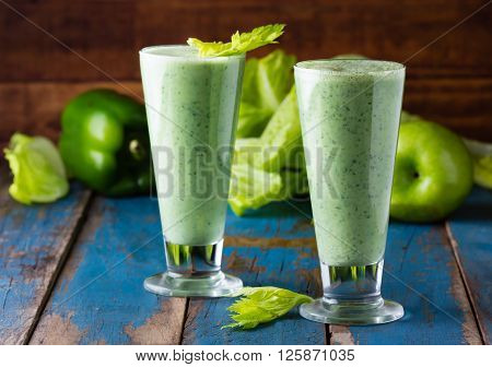 Two glasses of green smoothie and fresh green vegetables and fruits on wooden blue background
