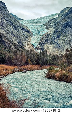 Briksdalsbreen glacier in Norway at autumn season. Mountain river from melted ice on foreground.