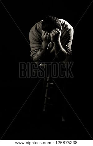 A man hides his face in angst against a black background