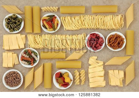 Healthy italian pasta collection with coloured varieties forming an abstract background over natural hemp paper background. 