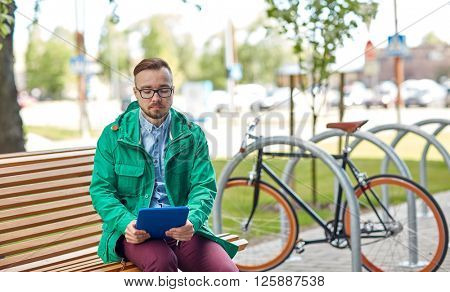 people, style, technology and lifestyle - sad young hipster man with tablet pc and fixie bike sitting on bench in city