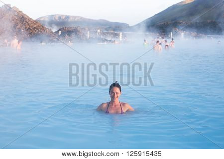 Woman relaxing in geothermal spa in hot spring pool in Iceland. Girl enjoying bathing in a blue water lagoon with famous healing mud.