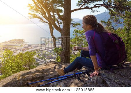 girl hiker with a backpack and trekking pole sitting and looking on Romsdalsfjorden and Andalsnes Norway