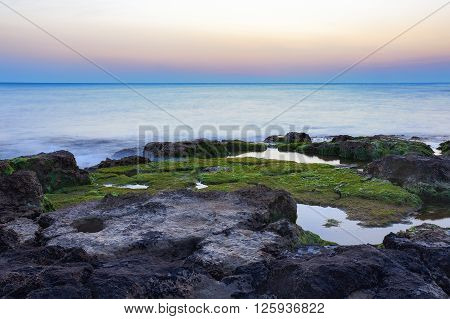 Sunset at Punta Secca Beach with rocks and green seaweeds in Santa Croce Camerina Sicily Italy