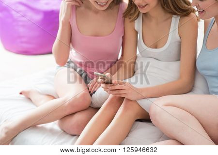Involved in net. Cheerful beautiful nice girls using smartphone and sitting on the bed while having henparty