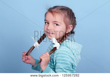 Smiling kid girl 3-4 year old posing over blue. Wearing blue striped hoodie. Looking at camera.