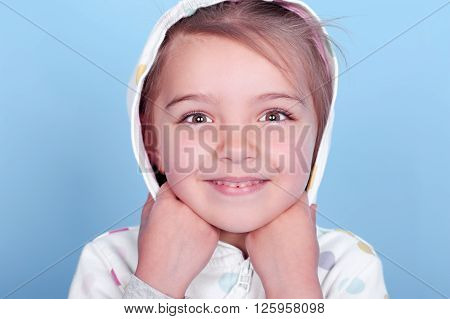 Smiling little girl wearing white hoodie with polka dots over blue. Posing in room. Looking at camera. Close up portrait.