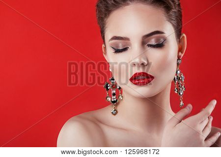 Beautiful model girl on a red background big earrings big portrait smile on face red lips . The beauty of a  woman . The picture was taken in a studio .