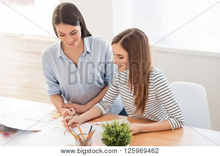 Involved in process. Positive charming nice girls sitting at the table and discussing project while feeling content