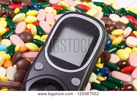 Glucose meter and heap of colorful medical pills capsules concept of treatment diabetes and health care