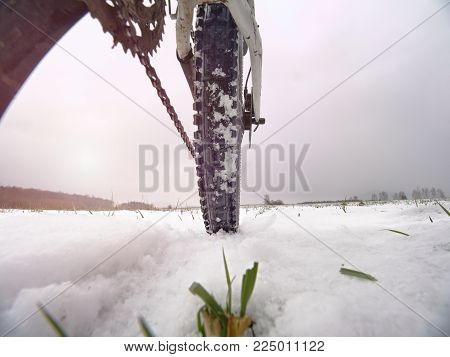Rear wheel detail of mtb. Snow flakes melting on dark off road tyre. Winter weather in the field.