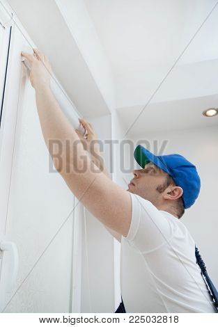 Handsome handyman installing cassette roller blinds at home.