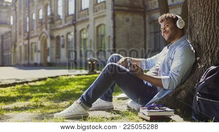 Male In Headphones Sitting On Grass And Leaning Against Tree, Listening To Music, Stock Footage